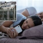 Uma mulher verifica o telefone na cama enquanto seu parceiro dorme ao lado dela.