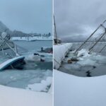 Um grande iate coberto de neve atracou próximo a um barco parcialmente submerso, cercado por gelo e neve no porto.
