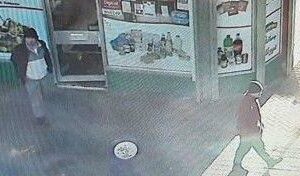 Nova CCTV divulgada em busca de assassino foragido A imagem do CCTV mostra dois homens passando por uma pequena loja. Um homem usa chapéu preto, casaco preto, calça cinza e camisa pólo. Outro usa o que parece ser uma jaqueta vermelha e um chapéu escuro.