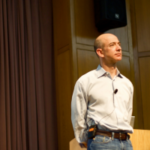 Jeff Bezos, fundador da Amazon, subiu no palco olhando para o público. Close dele, ele está vestindo camisa de cor clara, cinto e calça jeans. Suas mãos estão atrás das costas. O fundador da Amazon, Jeff Bezos, nega postagem da Polymarket sobre seu suposto conselho