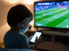 O jogo problemático é maior entre aqueles expostos ao jogo quando crianças Uma fotografia que captura a silhueta de uma criança por trás, sentada em um sofá, segurando um smartphone brilhante nas mãos. O jogo problemático é maior entre aqueles expostos ao jogo quando crianças