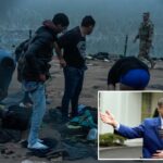 Os migrantes trocam de roupa na margem do rio, enquanto uma figura de autoridade dos EUA está por perto, com arame farpado ao fundo.