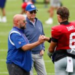 O técnico do Giants, Brian Daboll, dá um soco no quarterback Jaxson Dart, com o proprietário John Mara atrás deles, em um campo de futebol.