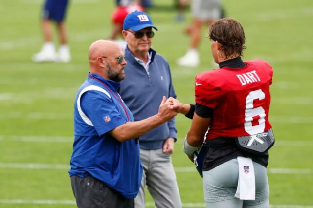 O que Brian Daboll está dizendo aos treinadores sobre a O técnico do Giants, Brian Daboll, dá um soco no quarterback Jaxson Dart, com o proprietário John Mara atrás deles, em um campo de futebol.
