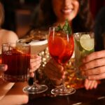 Amigos tilintando copos com coquetéis frescos no bar, closeup