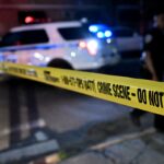 Carro de polícia com luzes piscando atrás da fita amarela da cena do crime que diz