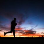 Uma silhueta de corredor contra o céu noturno enquanto o sol se põe.