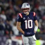 O jogador do New England Patriots, Mac Jones, com a camisa 10, com as mãos em uma bolsa, usando capacete e olhando para baixo.