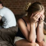 Homem irritado e mulher sentados num sofá e discutindo.