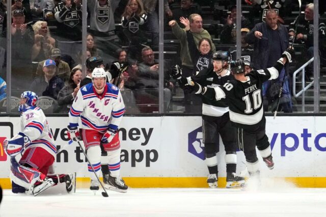 O ala direito do Los Angeles Kings, Adrian Kempe, segundo a partir da direita, comemora seu gol com o ala direito Corey Perry, à direita, enquanto o goleiro do New York Rangers, Jonathan Quick, à esquerda, e o centro JT Miller aguardam durante o primeiro período de um jogo de hóquei da NHL na terça-feira, 20 de janeiro de 2026, em Los Angeles.