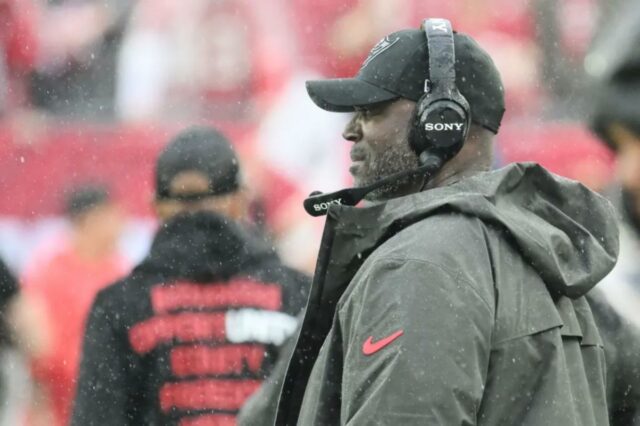 Todd Bowles demite vários treinadores em grande reforma dos Buccaneers O técnico do Tampa Bay Buccaneers, Todd Bowles, usando um fone de ouvido e um boné preto com logotipo, assistindo da linha lateral.