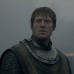 Um homem de armadura senta-se em cima de um cavalo em um campo de batalha.