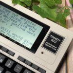 Um telefone idiota, uma câmera instantânea e um tablet e-reader dispostos em um fundo roxo com texto de colagem escrito 'DUMB'.