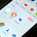 Mascote do Android 16 usando óculos escuros azuis com os braços levantados, cercado por ícones de aplicativos