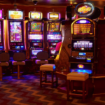 Mais de US$ 3 milhões supostamente ganhos em fundos fraudulentos de subsídios para jogos de azar. Fileira de caça-níqueis de cassino bem iluminadas dentro de um local de jogo, com bancos posicionados na frente de cada máquina e displays digitais coloridos brilhando em uma sala mal iluminada.