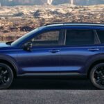 Um Mazda CX-5 2026 vermelho estacionado em uma calçada com vista para o porto