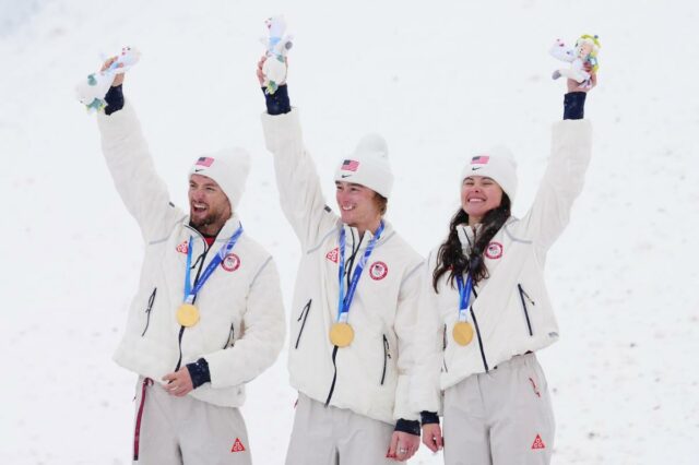 Os esquiadores de estilo livre Christopher Lillis, Kaila Kuhn e Connor Curran, dos Estados Unidos, comemoram a conquista da medalha de ouro enquanto Mengtao Xu, da China, assiste durante as Finais Aéreas de Equipes Mistas.