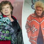 Mick Jagger com jaqueta estampada azul e camisa rosa, com as mãos nos bolsos, olhando para frente.