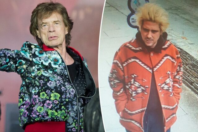 Mick Jagger com jaqueta estampada azul e camisa rosa, com as mãos nos bolsos, olhando para frente.