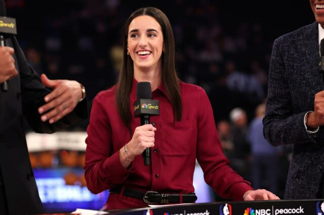 Caitlin Clark dá uma perspectiva otimista enquanto as negociações do Caitlin Clark sorri enquanto segura um microfone com o logotipo da NBC Sports, em um palco com outras pessoas, falando em um evento.