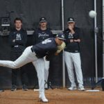 O arremessador do New York Yankees, Carlos Lagrange # 84, arremessa durante o treinamento de primavera com quatro treinadores observando ao fundo.