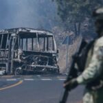 Um soldado monta guarda ao lado de um veículo carbonizado após este ter sido incendiado em Cointzio, estado de Michoacán, México, após a morte do líder do Cartel da Nova Geração de Jalisco, Nemesio Rubén Oseguera Cervantes, conhecido como “El Mencho”.