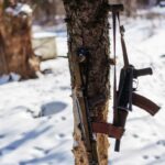 Dois rifles de assalto Kalashnikov pendurados em uma árvore em uma paisagem nevada.