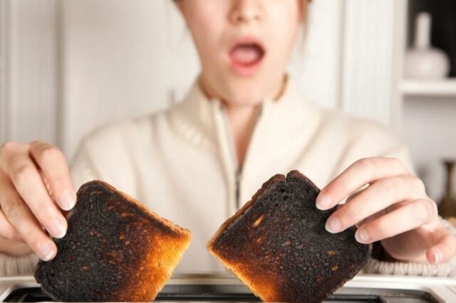 Uma mulher com a boca aberta de surpresa segura duas fatias de torrada queimada em uma torradeira.