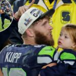 Cooper Kupp, do Seattle Seahawks, com boné e camisa de campeonato, segurando sua filha com sua esposa Anna Croskrey parcialmente visíveis atrás dele.