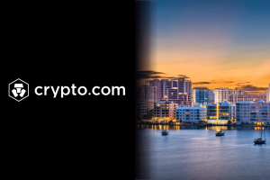 Crypto.com enfrenta processo na Flórida por supostas apostas esportivas ilegais Logotipo e nome da Crypto.com em branco sobre fundo preto ao lado do horizonte de uma cidade à beira-mar ao pôr do sol com arranha-céus iluminados e barcos em águas calmas. Crypto.com enfrenta processo na Flórida por supostas apostas esportivas ilegais
