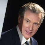 O governador da Califórnia, Gavin Newsom, falando ao microfone, apontando com o dedo indicador direito.