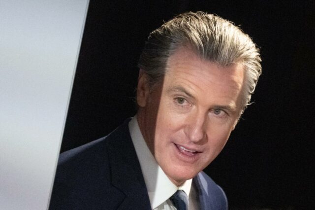 O governador da Califórnia, Gavin Newsom, falando ao microfone, apontando com o dedo indicador direito.