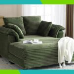 Espreguiçadeira de veludo cotelê verde com almofadas, manta de malha branca e livro com xícara de chá.