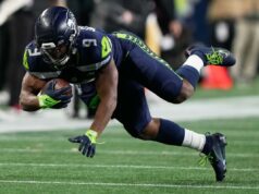 Esta é a aposta inicial mais direcionada para o Super Bowl 2026 Um jogador do Seattle Seahawks com uniforme azul escuro correndo com a bola de futebol durante um jogo.