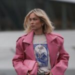 PARIS, FRANÇA - 25 DE JANEIRO: Constance Jablonski usa longos cabelos loiros ondulados com uma parte central, brincos de argola de metal, uma bolsa clutch de couro preta, uma jaqueta preta grande com listras jacquard com logotipo PATOU tonal, gola de couro texturizada e detalhes de fivela de metal em camadas sobre um top preto, uma minissaia combinando, bota skinny de couro preto brilhante, fora de Patou, durante a Paris Fashion Week - Moda masculina outono / inverno 2026-2027, em 25 de janeiro de 2026 em Paris, França (Foto de Edward Berthelot/Getty Images)