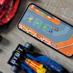 Mascote do Android segurando um controlador de jogo emergindo da tela de um smartphone e ícones de jogos coloridos flutuando.