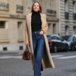 Jennifer Casimiro é vista vestindo um suéter creme de gola alta tricotado com detalhes volumosos de babados nos ombros da Zara; calça preta de cintura alta e silhueta afunilada, apertada nos tornozelos da Zara; sapatos pretos com cadarço e salto bloco, com detalhes de pompom nos tornozelos da Gucci; a pequena bolsa clutch preta Suede Varenne com formato retangular e marca dourada em relevo da Jimmy Choo; óculos de sol retangulares pretos grandes da MiuMiu; brincos com punho de ouro da Zara; seu cabelo preto está solto com uma parte central em 19 de setembro de 2025 em Hamburgo, Alemanha.