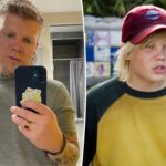 Blake Garrett vestindo uma camiseta cinza e segurando um telefone na frente dele.