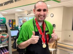 Fãs na Geórgia fazem fila para o querido caixa da Publix, autista Michael Masterangelo no Publix, vestindo camisa verde, avental preto e medalha da Special Olympics, fazendo sinal de positivo.