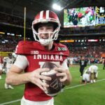 Fernando Mendoza, quarterback do Indiana, sorri enquanto segura uma bola de futebol.