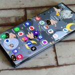 Um homem parado ao lado de um smartphone gigante com um balde e um esfregão em um fundo azul.