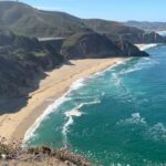 Grey Whale Cove State Beach, no condado de San Mateo, Califórnia, mostrando ondas quebrando contra a costa rochosa abaixo de um penhasco alto com um prédio no topo.