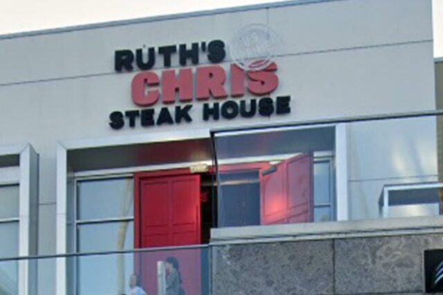 Ruth's Chris Steak House com entrada dupla vermelha e duas pessoas em pé em uma varanda abaixo do restaurante.