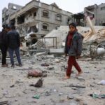 Um menino palestino deslocado senta-se sobre os escombros e escombros depois que um avião israelense atacou uma casa de cinco andares na noite passada, em Khan Yunis, sul da Faixa de Gaza, em 6 de fevereiro de 2026.