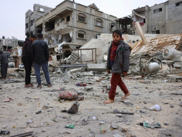 Um menino palestino deslocado senta-se sobre os escombros e escombros depois que um avião israelense atacou uma casa de cinco andares na noite passada, em Khan Yunis, sul da Faixa de Gaza, em 6 de fevereiro de 2026.