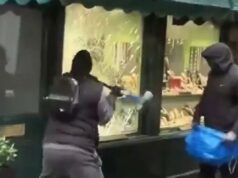 Ladrões de momentos selvagens quebram vitrines de joalheria em rua que ficou famosa por ‘Ted Lasso’ Dois ladrões mascarados assaltando uma joalheria, um quebrando a vitrine com uma ferramenta, o outro segurando uma bolsa azul.