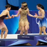 A partir da esquerda, Amber Glenn e a equipe de dança no gelo Madison Chock e Evan Bates comemoram a conquista da medalha de ouro após o evento da equipe de patinação artística nos Jogos Olímpicos de Inverno de 2026, em Milão, Itália, domingo, 8 de fevereiro de 2026. (AP Photo/Natacha Pisarenko)