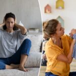 Uma mãe sentada em um sofá cobre os ouvidos de frustração quando seu filho passa correndo por ela.