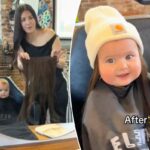 Uma mulher segurando extensões de cabelo em frente a um espelho, com um bebê com uma capa de barbeiro refletido no espelho.
