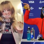 Uma pessoa com uma jaqueta esportiva branca e azul segura uma medalha olímpica.